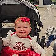 Mckenna is registered to the contest to win money with this photo: baby, child, stroller, headband, red_bow, festive_clothing, holiday, christmas, balloons, smiling, white_shoes, red_pants, indoor, cute, happy, person, toddler, decorations, celebration, sitting
