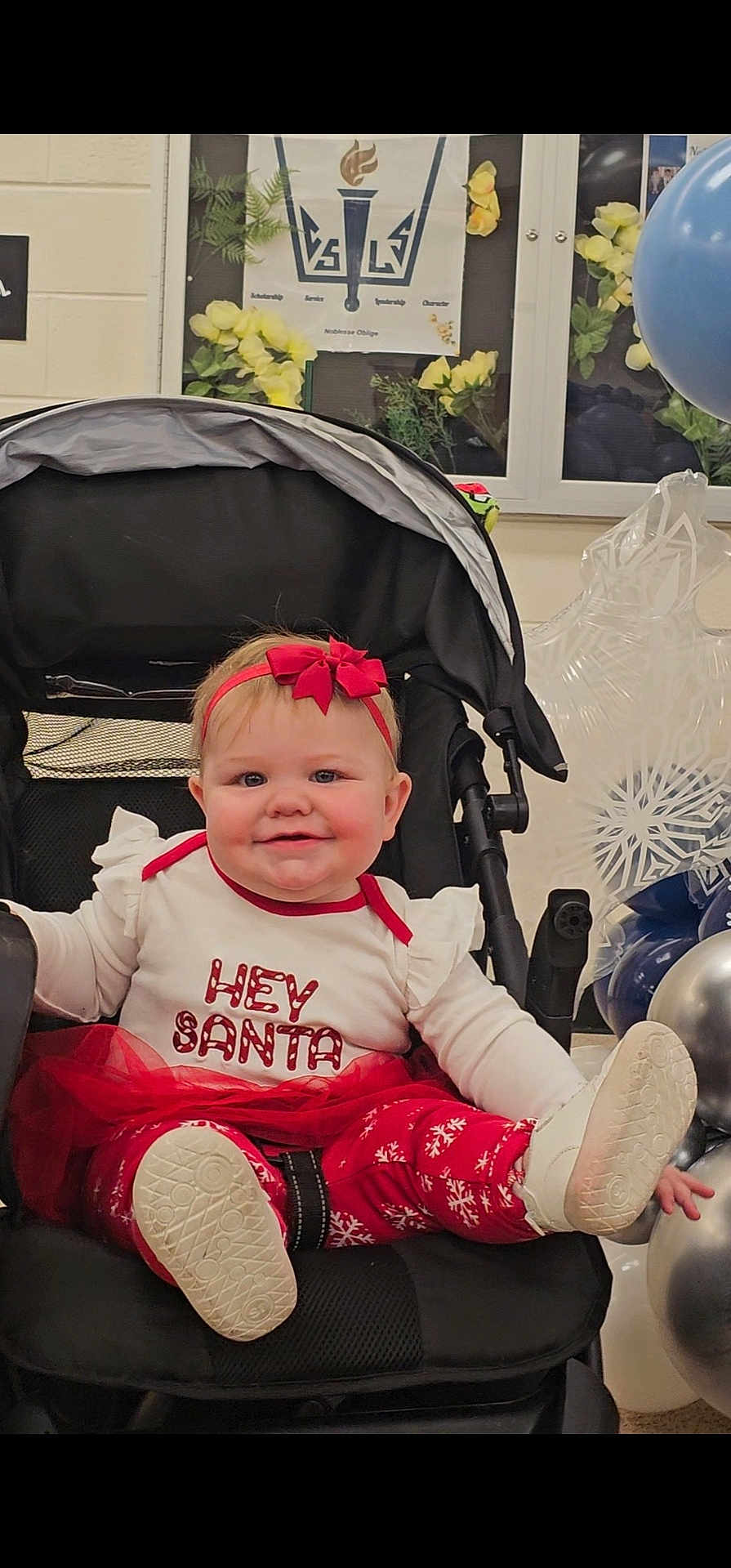 Mckenna is registered to the contest to win money with this photo: baby, child, stroller, headband, red_bow, festive_clothing, holiday, christmas, balloons, smiling, white_shoes, red_pants, indoor, cute, happy, person, toddler, decorations, celebration, sitting