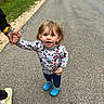 toddler, child, holding_hands, walking, road, suburban, grass, house, casual, blue_crocs, patterned_shirt, adult_hand, smiling, outdoor, person, footwear, sidewalk, nature, happy, daylight