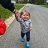 child, toddler, smiling, walking, holding_hand, adult_hand, road, sidewalk, grass, trees, house, blue_shoes, patterned_shirt, outdoor, daylight, casual_clothing, person, joy, nature, suburban