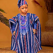 Abraham joined the competition — help win amazing prizes! child, traditional_clothing, hat, beads, blue, maroon, striped, standing, portrait, indoor, decor, plant, woven_mat, serious_expression, black_shoes, cultural, fashion, person, young, accessory