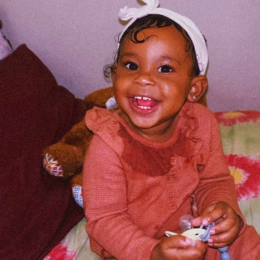 Milani is registered to the contest to win money with this photo: baby, bed, bodypart, clothing, couch, cushion, face, finger, furniture, hand, happy, hat, head, homedecor, laughing, mouth, person, photography, portrait, smile