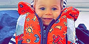 Maëlio participe au concours pour gagner de l'argent avec cette photo : toddler, child, life_jacket, orange, smiling, boat, window, sky, blue_eyes, striped_shirt, happy, young_child, safety, clothing, seat, indoor, portrait, casual, cute, playful