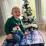 Maëlio a rejoint le concours — aidez-le/la à gagner de superbes lots ! toddler, child, smiling, green_sweater, santa_claus, christmas_tree, ornaments, gift_box, indoor, window, curtains, holiday, festive, kneeling, happy, jeans, present, decorations, silver_star, floor