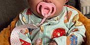 Haisley is registered to the contest to win money with this photo: baby, pacifier, bow, pajamas, donut_pattern, couch, cushion, orange, blue, pink, infant, child, indoor, cute, soft_toy, hand, face, headband, smiling, comfort