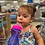 Athena is registered to the contest to win money with this photo: toddler, child, sippy_cup, dress, turtle_pattern, shopping_cart, store, aisle, hair_bun, cute, drinking, plastic_cup, colorful, young_child, portrait, indoor, baby, person, clothing, retail