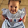 child, girl, smiling, braids, hair_bows, dress, blue_dress, checkered_pattern, usa_text, floor_tiles, indoors, holding_dress, cute, portrait, young_child, happy, fashion, casual, person, toddler