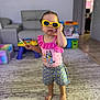 Athena joined the competition — help win amazing prizes! toddler, child, indoor, sunglasses, pink_clothing, shorts, barefoot, carpet, living_room, toy, furniture, playroom, cute, fashion, person, portrait, standing, colorful, casual, young_child