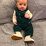 Levi is registered to the contest to win money with this photo: baby, child, infant, green_overalls, white_shoes, sitting, gray_blanket, soft_texture, cute, smiling, indoors, portrait, young_child, cozy, clothing, footwear, face, expression, hands, couch