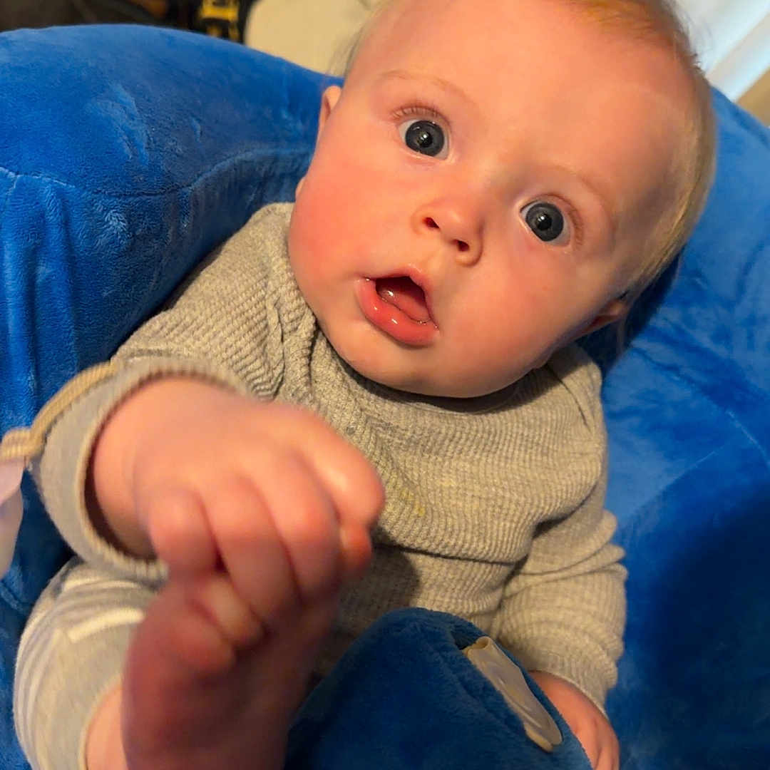 Grayson joined the competition — help win amazing prizes! baby, child, infant, blue_cushion, plush, indoor, curious, reaching, face, hand, foot, rosy_cheeks, seated, clothing, person, portrait, closeup, head, expression, eyewear