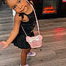 Antonella is registered to the contest to win money with this photo: child, girl, black_dress, pink_purse, bow, letter_a, purple_shoes, wooden_floor, fireplace, fish_tank, decor, home_interior, smiling, posing, person, young_child, cute, indoor, standing, flooring