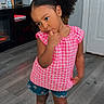 child, girl, indoor, curly_hair, pigtails, pink_top, denim_shorts, sandals, wooden_floor, door, cabinet, thoughtful, cute_pose, standing, person, clothing, flooring, hair_style, casual_wear, home_interior