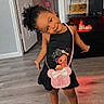 child, girl, smiling, dress, purse, indoor, floor, fish_tank, television, wooden_floor, black_dress, purple_shoes, curly_hair, door, cabinet, lighting, home_interior, playful, cute, standing