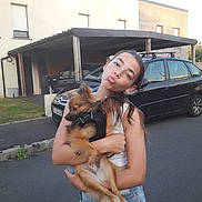 Aïko a rejoint le concours — aidez-le/la à gagner de superbes lots ! girl, child, dog, pet, holding, street, car, house, carport, summer, casual_clothing, denim_shorts, white_tank_top, playful, portrait, outdoor, animal, young, fun, daytime