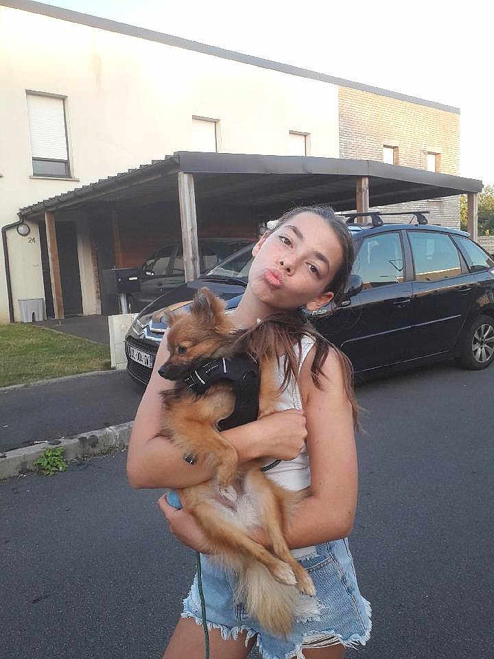 Aïko a rejoint le concours — aidez-le/la à gagner de superbes lots ! girl, child, dog, pet, holding, street, car, house, carport, summer, casual_clothing, denim_shorts, white_tank_top, playful, portrait, outdoor, animal, young, fun, daytime