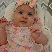 Luna joined the competition — help win amazing prizes! baby, child, infant, pink_dress, headband, flower, bow, cute, smiling, face, hand, soft_cushion, patterned_background, indoor, portrait, happy, young_child, apparel, closeup, person