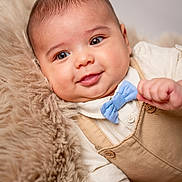 Maxime participe au concours pour gagner de l'argent avec cette photo : baby, infant, smile, face, blue_bow_tie, beige_overall, fluffy_blanket, cute, portrait, child, close_up, soft_texture, happy, young, indoors, skin, head, eyes, hand, clothing