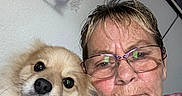 Boomer joined the competition — help win amazing prizes! dog, person, glasses, tie_dye_shirt, selfie, indoor, dreamcatcher, wall_decor, close_up, pet, fluffy_dog, face, portrait, casual, adult, home, cute, looking_at_camera, brown_hair, eyewear