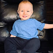 Atticus is registered to the contest to win money with this photo: child, toddler, smile, blue_shirt, black_pants, leather_chair, indoor, happy, sitting, face, young, cute, casual_clothing, barefoot, relaxed, portrait, furniture, home, comfort, light