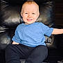 child, toddler, smile, blue_shirt, black_pants, leather_chair, indoor, happy, sitting, face, young, cute, casual_clothing, barefoot, relaxed, portrait, furniture, home, comfort, light