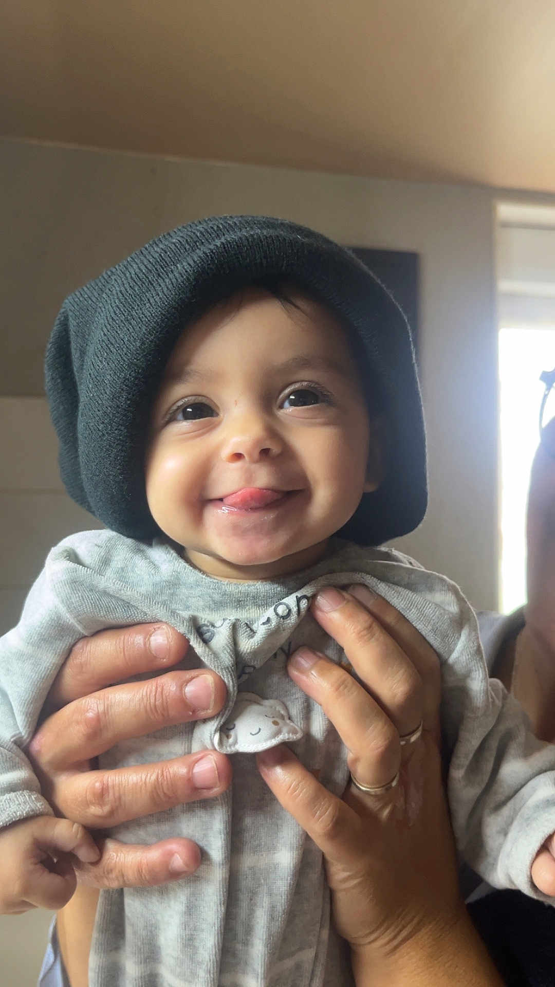 Maria participe au concours pour gagner de l'argent avec cette photo : baby, child, infant, smiling, tongue_out, knit_hat, hands, rings, gray_clothing, indoor, window, face, person, cute, playful, closeup, portrait, skin, happy, holding