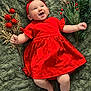 baby, infant, red_dress, headband, smiling, green_blanket, holiday_decor, red_berries, pine_branches, happy, cute, child, lying_down, festive, celebration, portrait, indoors, soft_texture, cheerful, adorable