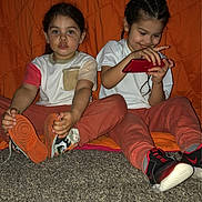 Andy joined the competition — help win amazing prizes! children, child, sibling, kids, portrait, sitting, carpet, indoors, orange_background, handheld_device, video_game, red_device, sneakers, shoes, casual_clothing, smiling, braids, family, photography, playtime