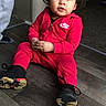 child, toddler, baby, portrait, sitting, indoors, red_tracksuit, sneakers, pigtails, smiling, face, curly_hair, fashion, sportswear, floor, wooden_floor, home, doorway, shoes, nike