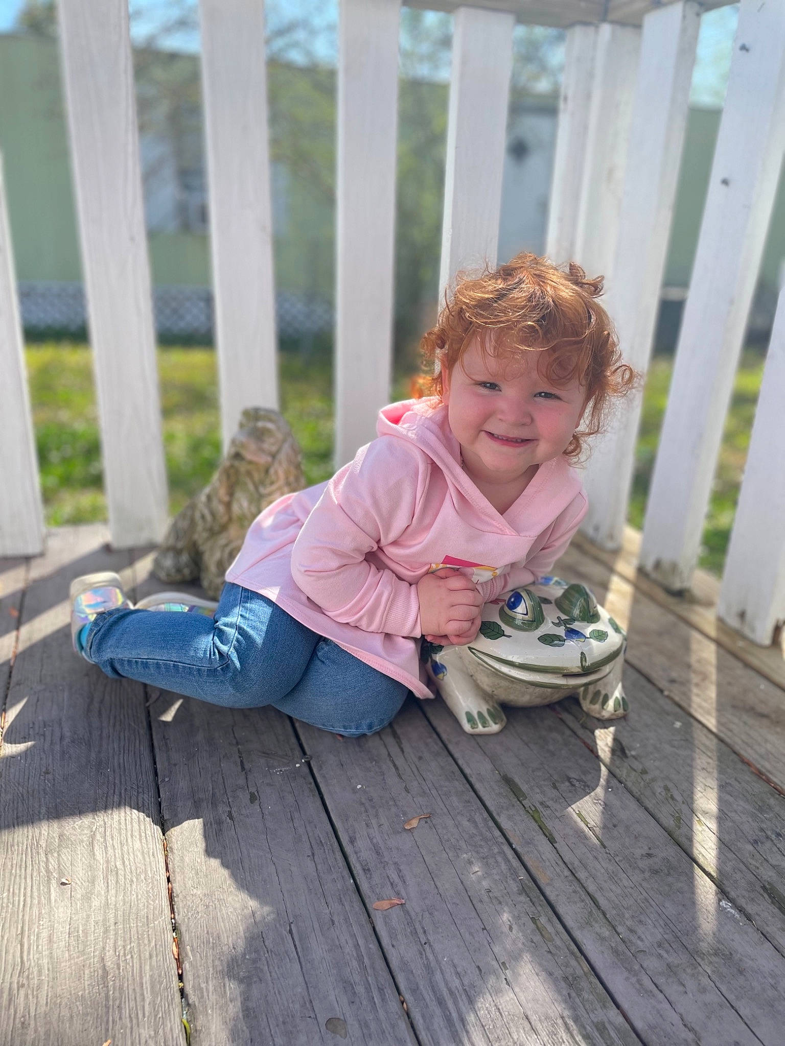Julie is registered to the contest to win money with this photo: baby_toddler_clothing, child, deck, fence, flooring, fun, grass, happy, hardwood, joy, leaf, leisure, mammal, person, shoe, sitting, smile, sneakers, standing, toddler