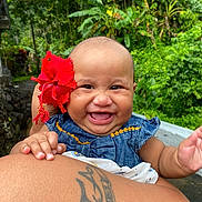 Aloralei joined the competition — help win amazing prizes! baby, child, smiling, flower, red_flower, denim_dress, tattoo, arm, outdoor, greenery, tropical, nature, happy, portrait, infant, cute, skin, person, holding, closeup