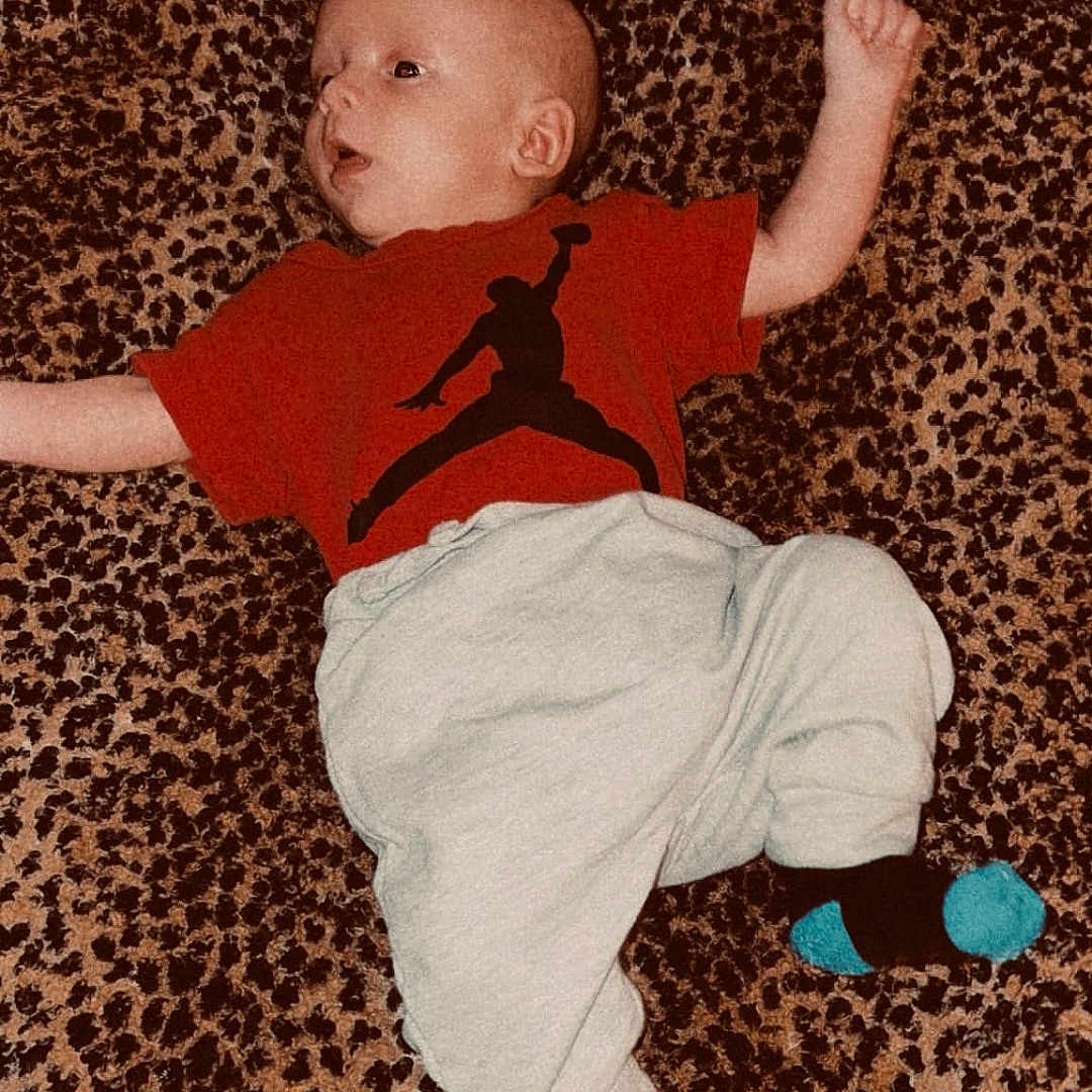 Grayson joined the competition — help win amazing prizes! baby, black_logo, blanket, blue_socks, casual_clothing, child, curious_expression, cute, human, indoor, infant, leopard_print, light_pants, lying_down, portrait, red_tshirt, relaxed, small_child, socks, soft_texture