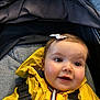 baby, child, yellow_jacket, stroller, bow, smiling, face, young_child, happy, cute, infant, outerwear, straps, closeup, person, portrait, headwear, seat, fabric, indoors