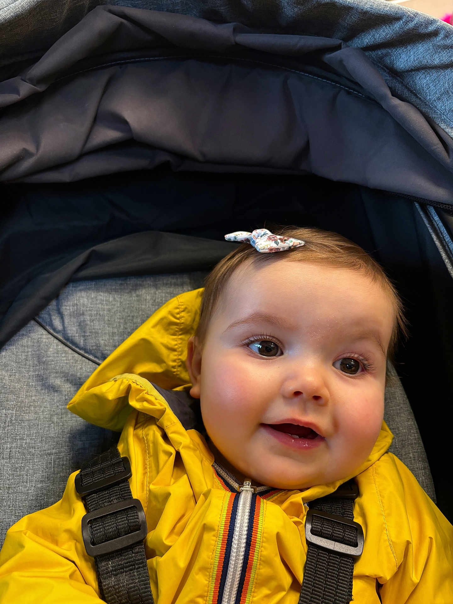 Garance participe au concours pour gagner de l'argent avec cette photo : baby, child, yellow_jacket, stroller, bow, smiling, face, young_child, happy, cute, infant, outerwear, straps, closeup, person, portrait, headwear, seat, fabric, indoors