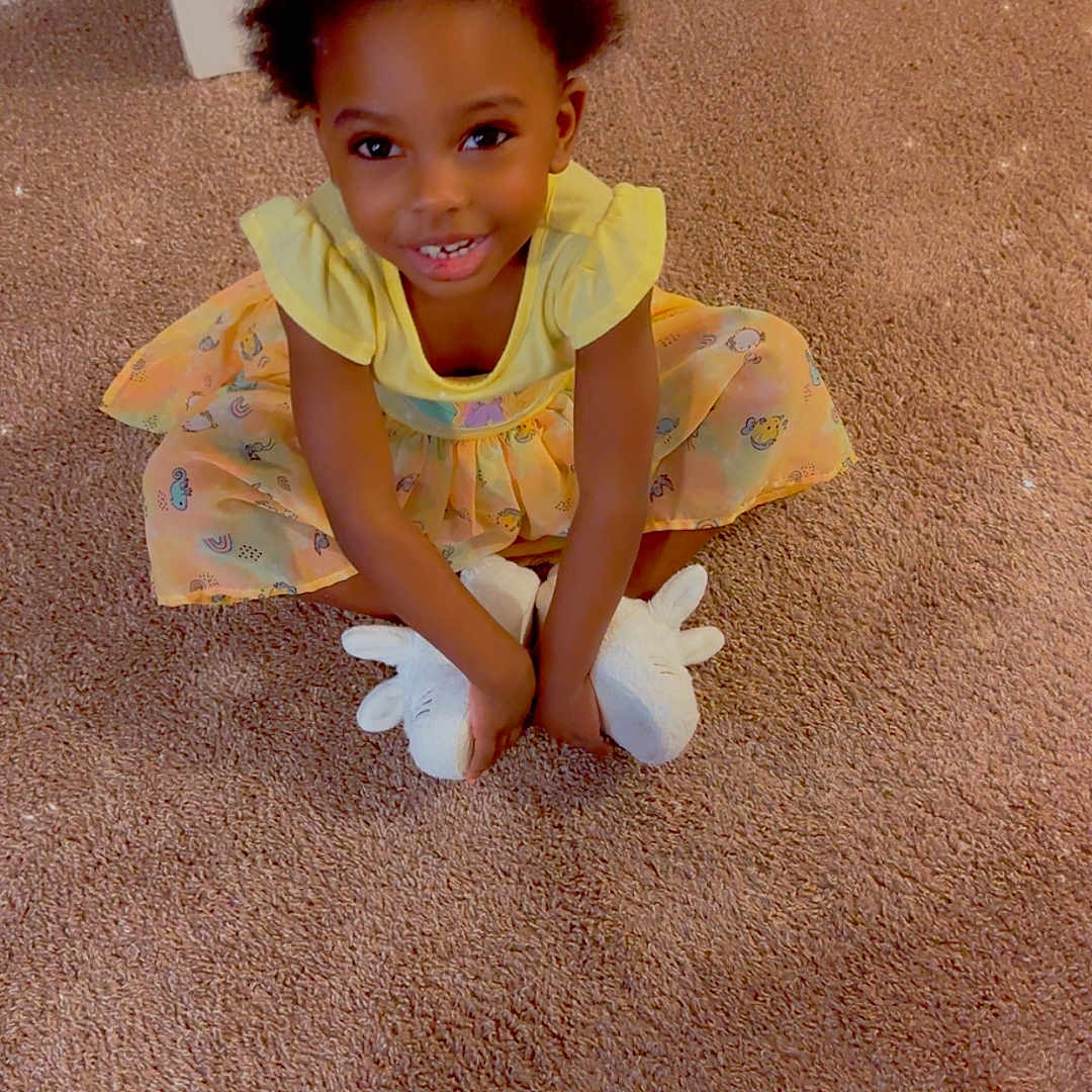 Jahli is registered to the contest to win money with this photo: carpet, child, cross_legged, curly_hair, cute, door, girl, happy, home, indoor, person, playful, plush_slippers, portrait, sitting, smiling, sparkle_effect, unicorn_slippers, yellow_dress, young