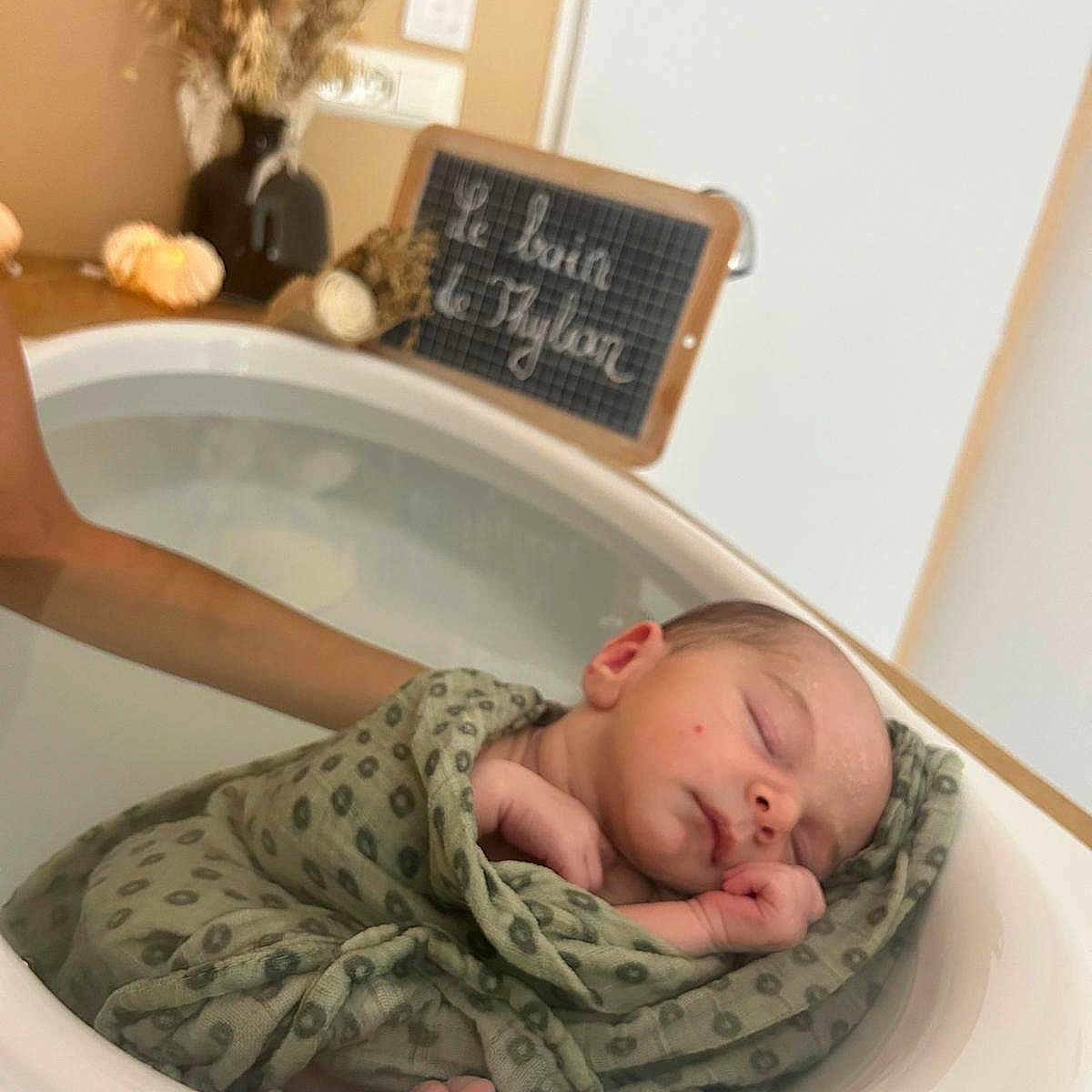 Thylian participe au concours pour gagner de l'argent avec cette photo : arm, baby, basin, blanket, chalkboard, cursive_text, dried_flowers, feet, hand, head, indoor, infant, newborn, peaceful, skin, sleeping, soft_light, swaddled, vase, water