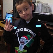 Loucas is registered to the contest to win money with this photo: child, boy, hoodie, indoor, computer, printer, desk, hand_gesture, holiday_sweater, christmas, cartoon, gift_box, furniture, room, smile, casual, short_hair, person, tile_floor, home
