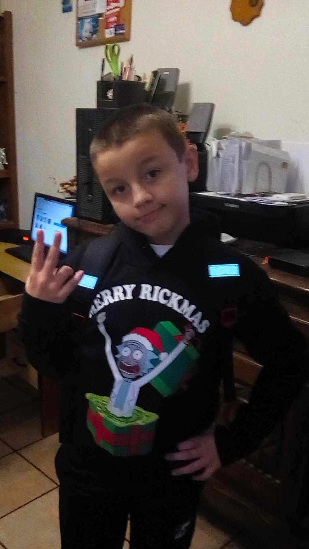 Loucas is registered to the contest to win money with this photo: child, boy, hoodie, indoor, computer, printer, desk, hand_gesture, holiday_sweater, christmas, cartoon, gift_box, furniture, room, smile, casual, short_hair, person, tile_floor, home