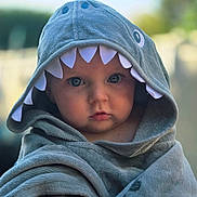 Manoë participe au concours pour gagner de l'argent avec cette photo : baby, child, hooded_towel, shark_costume, cute, portrait, blue_eyes, soft_texture, outdoor, blurred_background, infant, wrapped, face, expression, clothing, adorable, towel, young_child, closeup, headwear