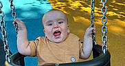 Lorenzo joined the competition — help win amazing prizes! baby, blue, child, colorful, fence, happy, open_mouth, outdoor, park, playground, playground_surface, seated, smiling, striped_shorts, sunlight, swing, swing_chains, toddler, trees, yellow