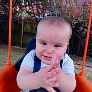 Lorenzo is registered to the contest to win money with this photo: baby, child, clapping, clothing, expression, fence, fun, garden, grass, happy, nature, outdoor, person, play, seat, smiling, summer, swing, trees, young