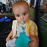 Lorenzo is registered to the contest to win money with this photo: baby, blond_hair, brown_eyes, child, close_up, couch, furniture, house, indoor, infant, looking_at_camera, pacifier, playpen, playroom, portrait, sitting, striped_clothing, toy, turquoise_toy, yellow_shirt