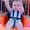 Lorenzo is registered to the contest to win money with this photo: arms, baby, child, expression, fun, grass, happy, harness, orange, outdoor, person, play, playground, reaching, seat, shorts, striped_shirt, summer, swing, trees