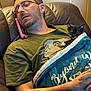 man, sleeping, phone, glasses, kitten, black_and_white_cat, blanket, chair, indoor, casual_clothing, beard, resting, closed_eyes, leather_chair, hands, relaxation, nap, domestic_animal, cute, cozy