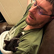 Oakley joined the competition — help win amazing prizes! man, glasses, sleeping, kitten, cat, blanket, couch, indoor, relaxing, beard, green_shirt, chain_necklace, pet, snuggling, comfort, resting, fur, paw, closeup, human
