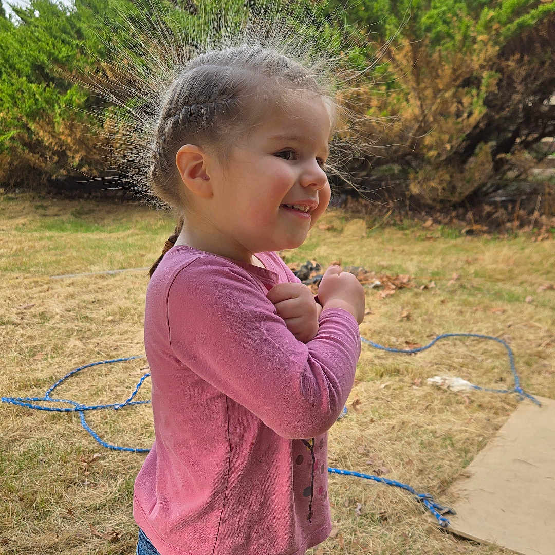 Sophia is registered to the contest to win money with this photo: braided_hair, casual_clothing, child, cute, daylight, fun, girl, grass, happy, jeans, nature, outdoor, pink_shirt, portrait, profile, shrubbery, smiling, standing, static_hair, young