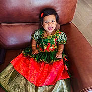 Sanmika Bodepudi is registered to the contest to win money with this photo: toddler, smiling, traditional_dress, green, red, gold, bracelet, necklace, hair_accessory, leather_chair, indoor, child, happy, portrait, cute, sitting, person, floor, jewelry, fashion