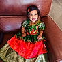 toddler, smiling, traditional_dress, green, red, gold, bracelet, necklace, hair_accessory, leather_chair, indoor, child, happy, portrait, cute, sitting, person, floor, jewelry, fashion