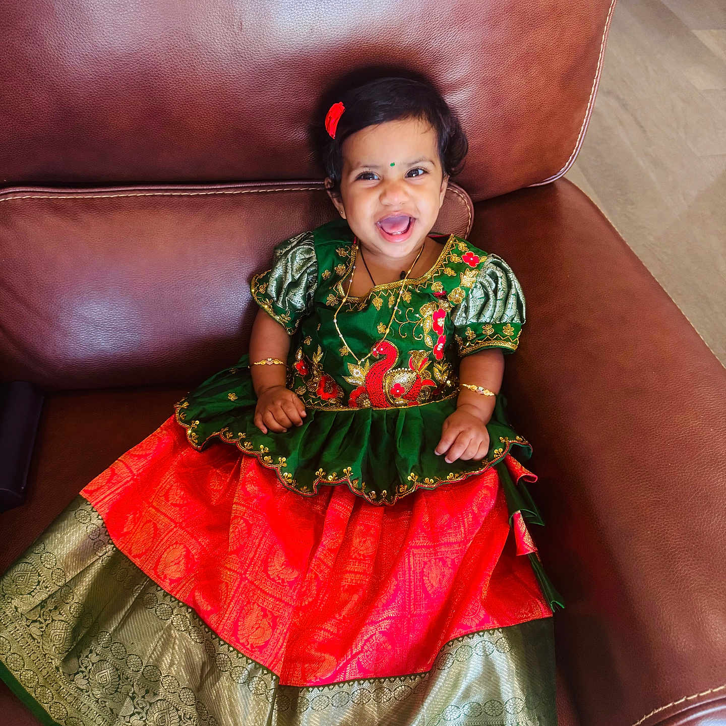 Sanmika Bodepudi is registered to the contest to win money with this photo: bracelet, child, cute, fashion, floor, gold, green, hair_accessory, happy, indoor, jewelry, leather_chair, necklace, person, portrait, red, sitting, smiling, toddler, traditional_dress