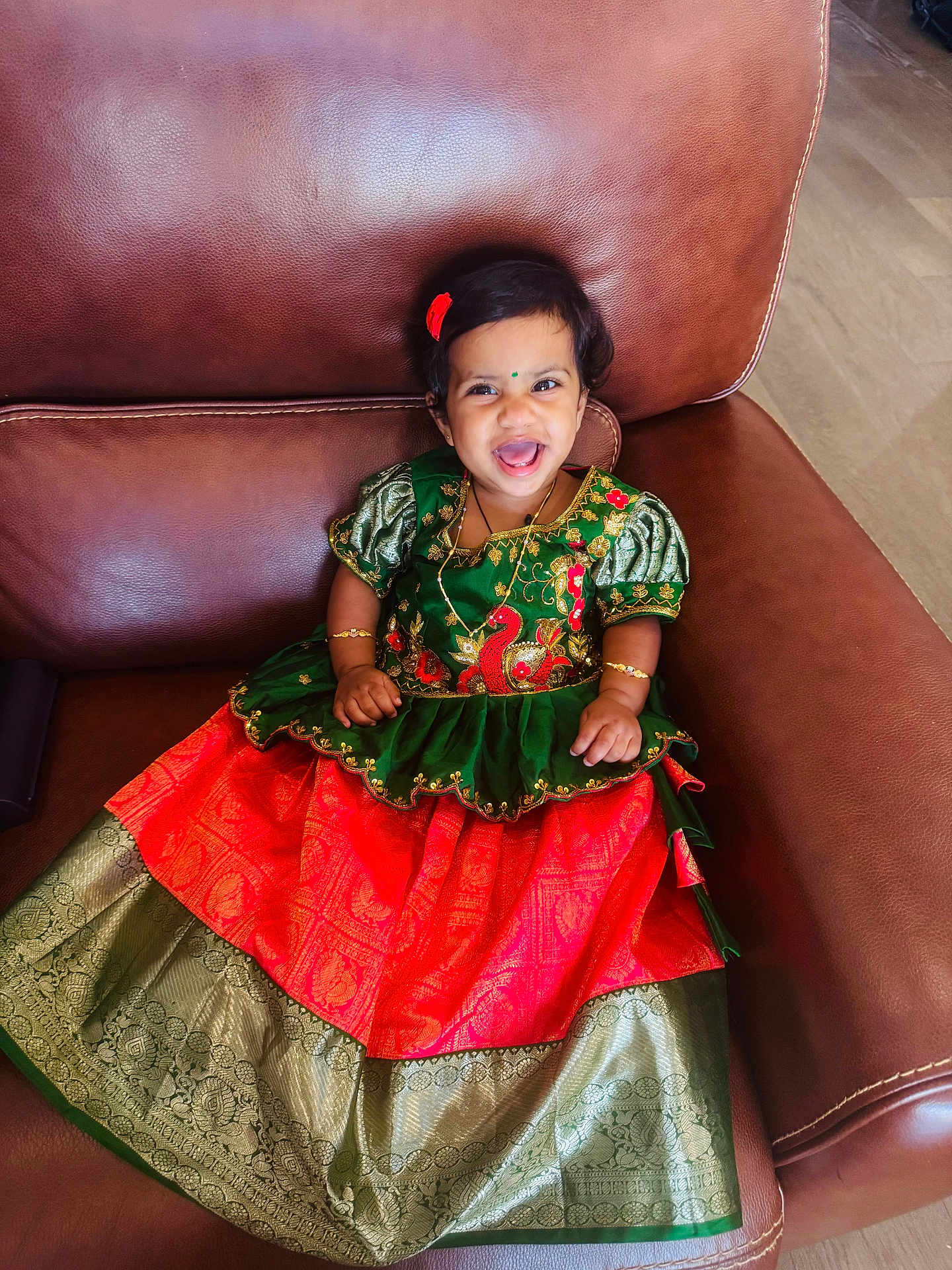 Sanmika Bodepudi is registered to the contest to win money with this photo: toddler, smiling, traditional_dress, green, red, gold, bracelet, necklace, hair_accessory, leather_chair, indoor, child, happy, portrait, cute, sitting, person, floor, jewelry, fashion