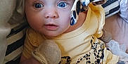 Eliana is registered to the contest to win money with this photo: baby, infant, headband, blue_eyes, mittens, yellow_clothing, tutu, striped_pillow, couch, face, person, cute, indoor, portrait, child, young, sitting, fabric, pattern, soft